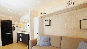 A compact living space with a kitchenette, a sofa with cushions, and a wooden wall.