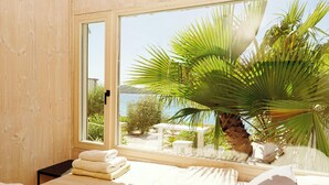 A room with a large window, a bed with white linens, and a view of a body of water and greenery outside.