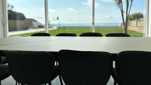 Une salle de conférence dotée d’une grande table et de chaises noires, offrant une vue sur un espace verdoyant et l’océan.