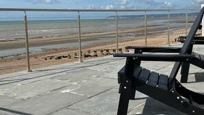 Une vue sur la plage depuis un balcon doté d’une rambarde en métal et d’une chaise noire.