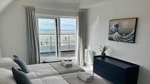 Une chambre avec deux lits, une vue sur la plage, un tableau représentant une vague et une commode bleu foncé.