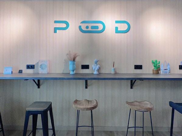 Zona de bar con mostrador que muestra el logotipo de POD, taburetes de bar y varios objetos decorativos.