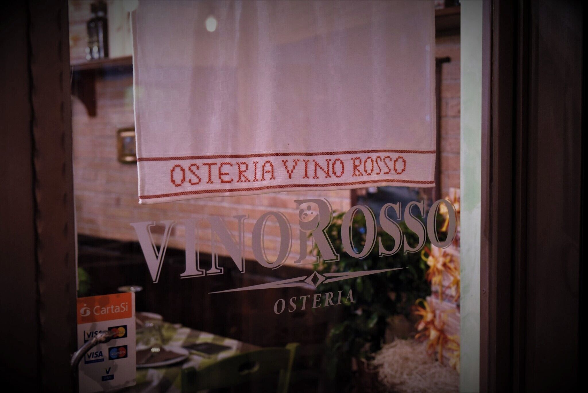 Une fenêtre sur laquelle on peut lire les mots « OSTERIA VINO ROSSO » et « VINO ROSSO », indiquant qu’il s’agit d’un restaurant.