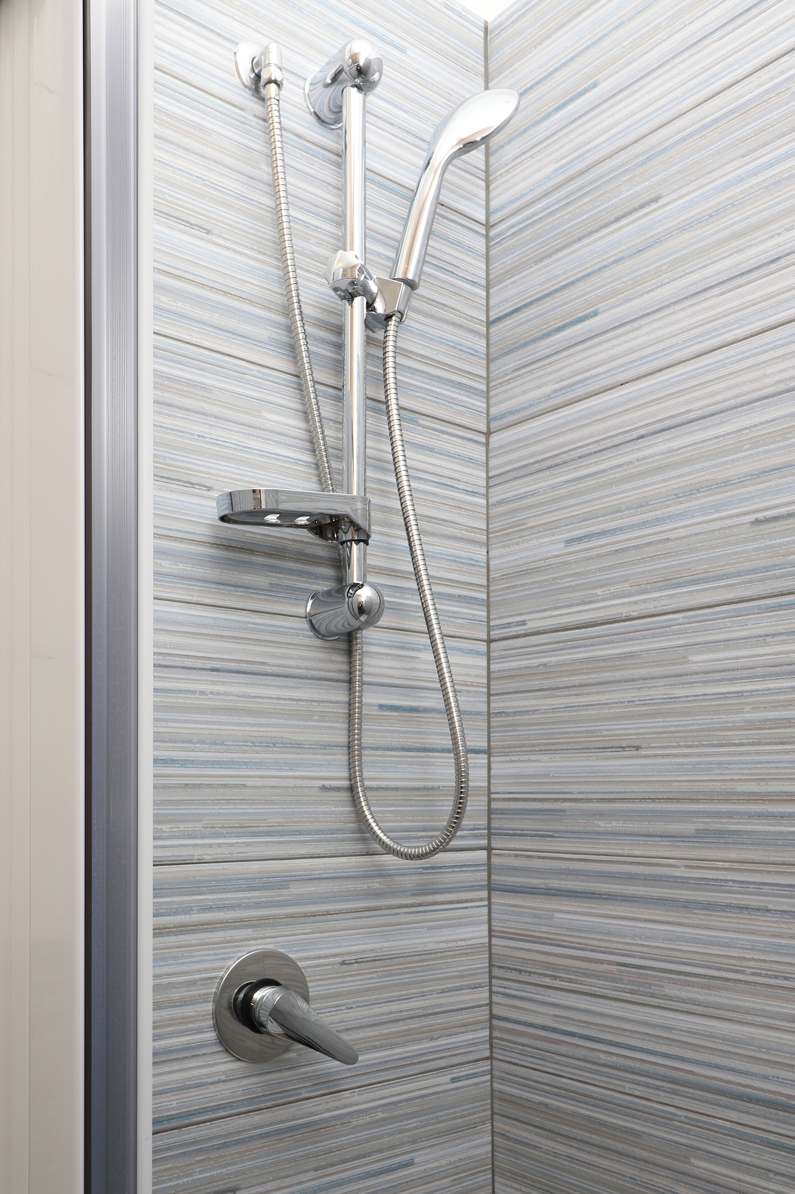 Eine Dusche mit Handbrause und Wandarmatur vor einer Wand mit Streifenfliesen.