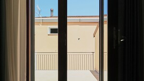 En åben skydedør, der fører ud til en balkon med flisegulv og en bygning i baggrunden.