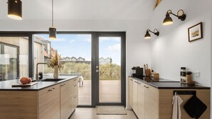 Eine moderne Küche mit einer großen Kochinsel, Holzschränken und Blick auf den Strand durch eine Glastür.
