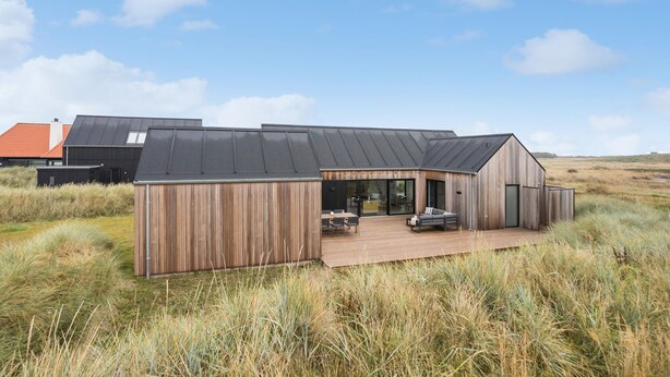 Ein modernes Haus mit Holzterrasse, großen Schiebegläsern und einer Flachdach.