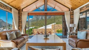 Amplia sala de estar con techo de madera, sofás de cuero, una mesa de centro y grandes ventanas con vistas a la montaña.