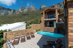 A two-story building with a swimming pool and outdoor seating area, surrounded by mountains. - Auberge Cape (Cape Town)
