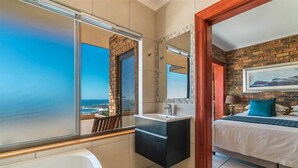 Un baño moderno con bañera, lavabo y espejo. Una ventana grande ofrece vistas al océano.