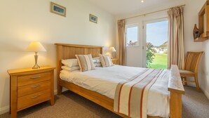Un dormitorio ordenado con una cama de madera, dos mesitas de noche con lámparas, una silla de madera y vistas a un paisaje verde a través de la ventana.