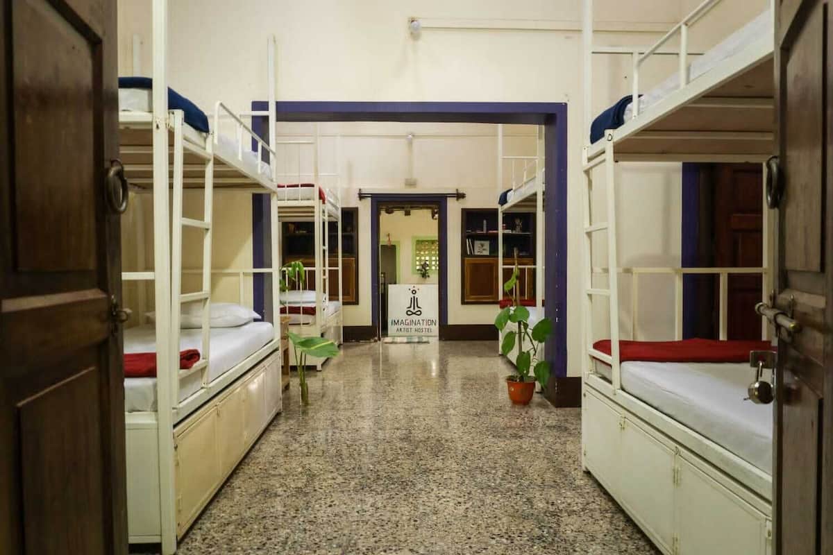 A hostel corridor with bunk beds, a sign for 'IMAGINATION ARTIST HOSTEL', and a potted plant.