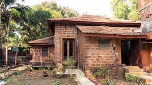 Une maison de campagne au toit recouvert de tuiles, aux murs en briques et dotée d’un petit jardin où poussent différentes plantes, ainsi que d’un sentier.