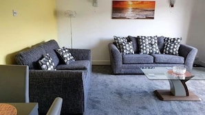 Ein Wohnzimmer mit zwei grauen Sofas, einem Couchtisch und einem Gemälde, das einen Sonnenuntergang zeigt.