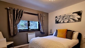 Ein Schlafzimmer mit einem großen Bett, einem Heizkörper, einem Fenster mit Vorhängen, einer Deckenleuchte und einem Wandbild.