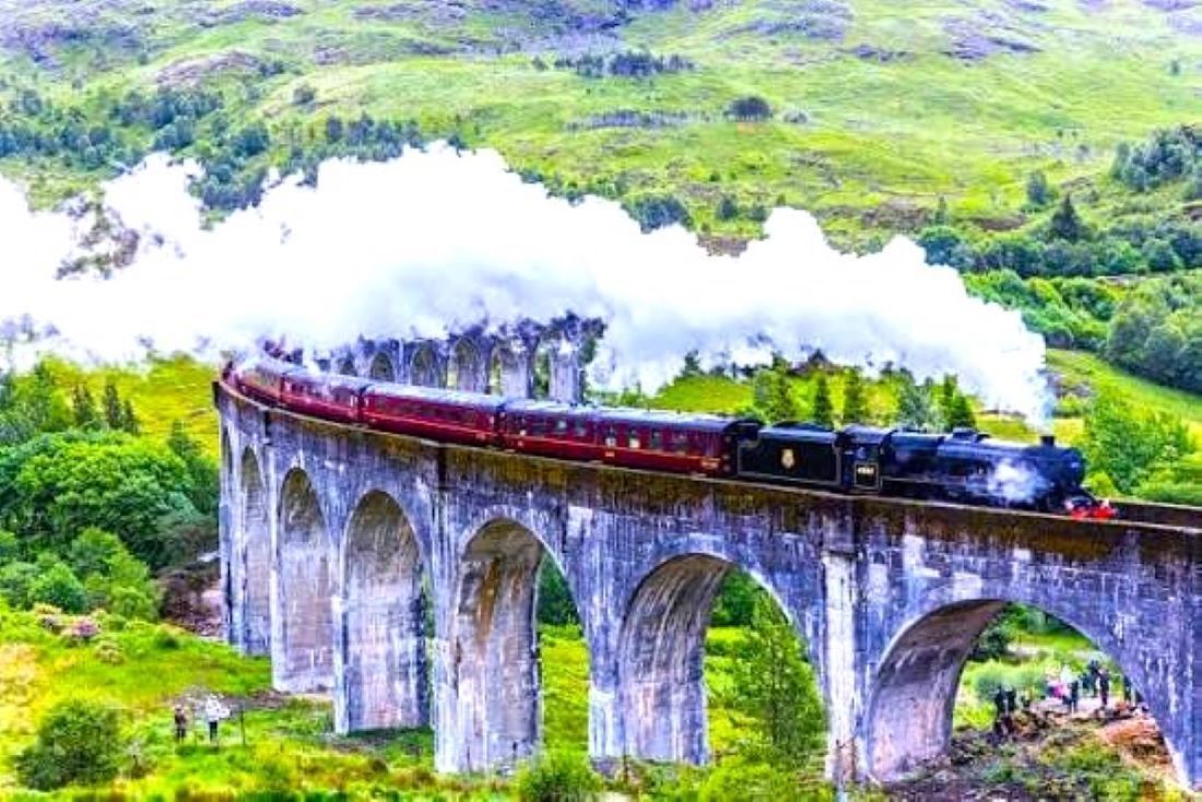 A steam train crossing a stone viaduct over a lush green valley.