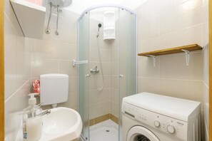 Une salle de bain compacte comprenant une douche à parois de verre, des toilettes, un lavabo avec distributeur de savon et un lave-linge.