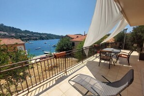 Un balcon donnant sur un lac où l’on peut admirer les bateaux, une table avec des chaises et une balustrade.