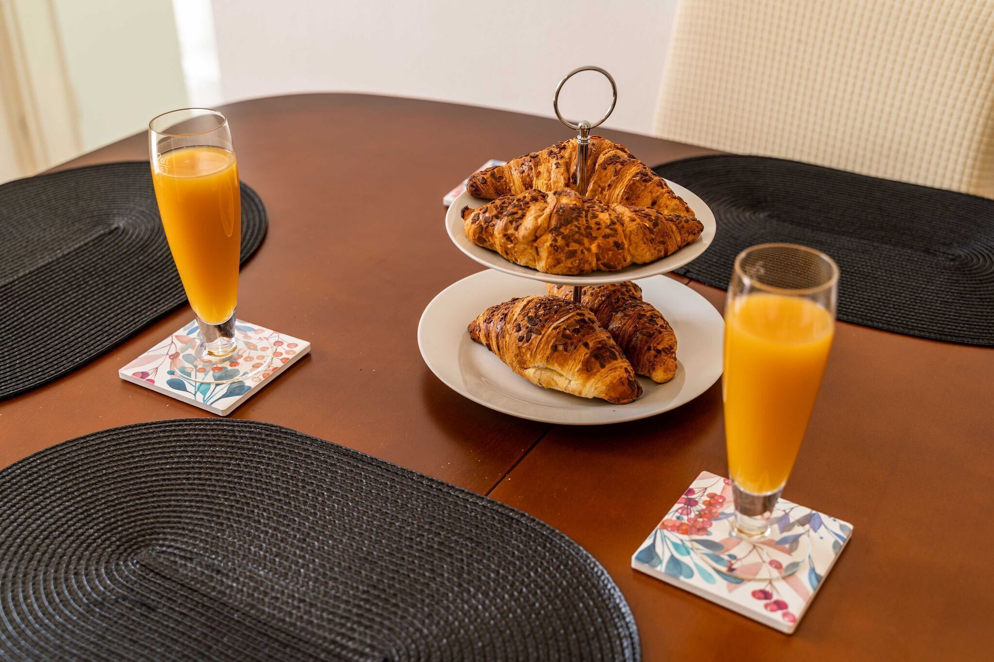 A table with two plates of croissants and two glasses of orange juice, each with a coaster.