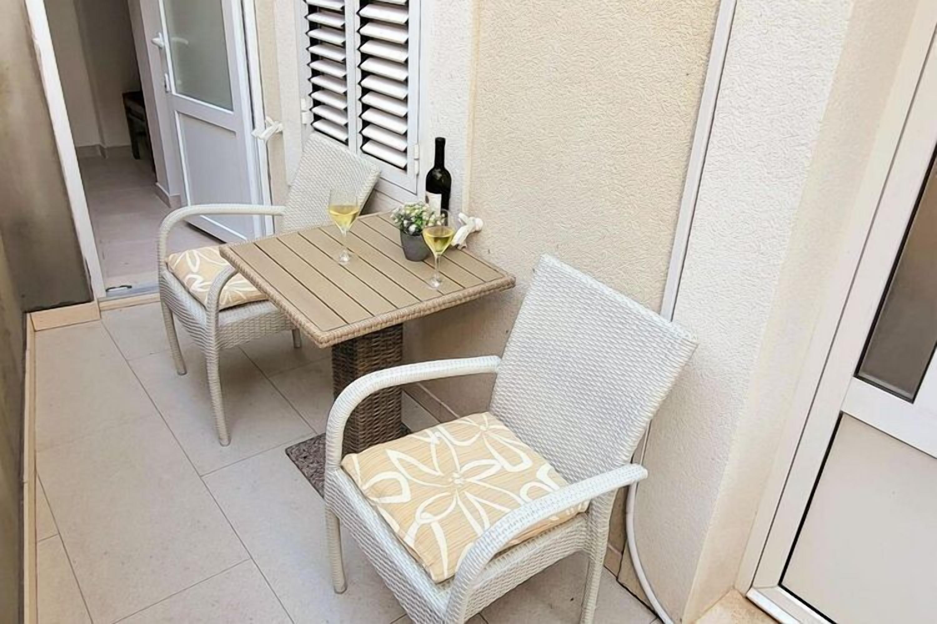 Un petit espace extérieur aménagé avec une table et deux chaises en osier, une bouteille de vin et une petite plante posée sur la table.