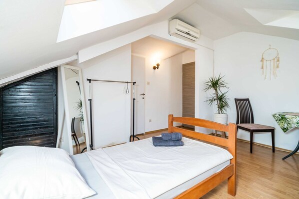 Un dormitorio con cama de madera, ventilador de techo, planta en maceta y un atrapasueños en la pared.
