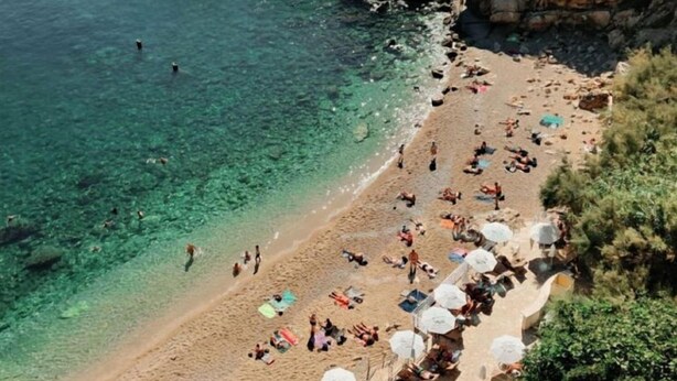 A beach with clear water, people sunbathing, and umbrellas.