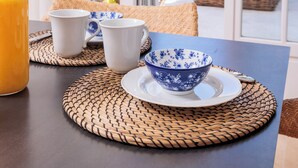 Una mesa de desayuno con una botella de jugo de naranja, dos tazas blancas y un cuenco azul y blanco sobre individuales tejidos.