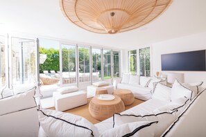 Una sala de estar moderna con muebles blancos, ventanas amplias y un ventilador de techo.