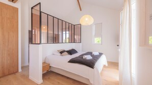 Un dormitorio con cama, suelo de madera, un ventanal grande y una lámpara colgante.
