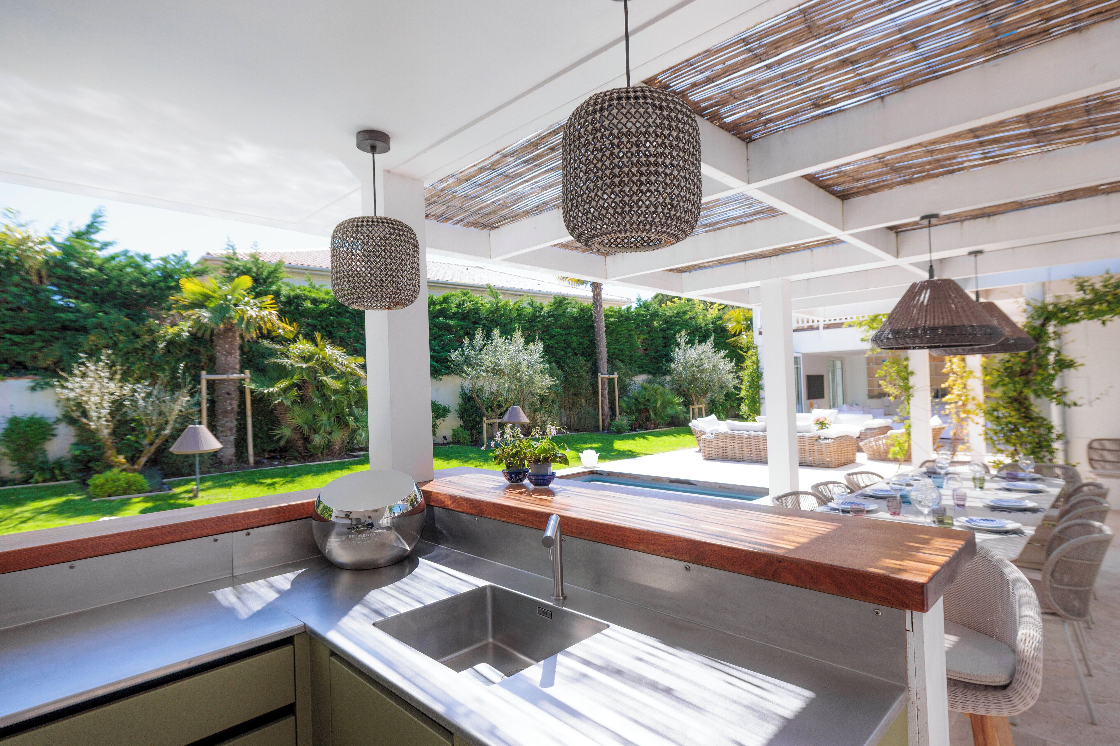 An outdoor kitchen with a built-in sink, wooden countertop, and hanging pendant lights.