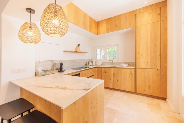 Una cocina moderna con armarios de madera, encimera de mármol y dos lámparas colgantes.
