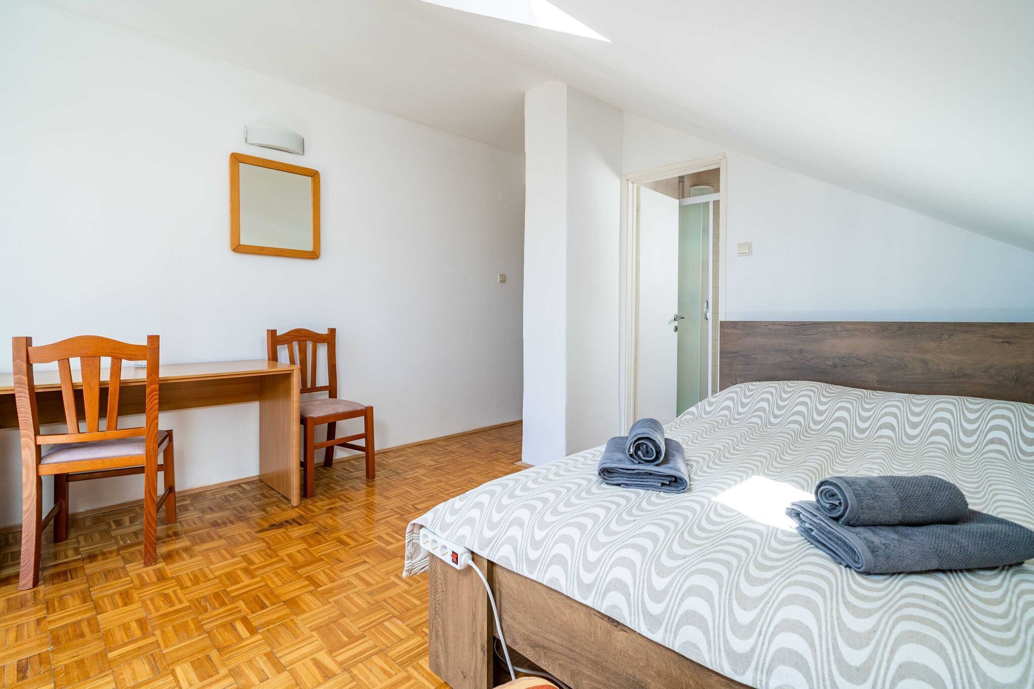 Ein Schlafzimmer mit einem Bett, zwei Holzstühlen, einem Schreibtisch und einem Spiegel an der Wand.