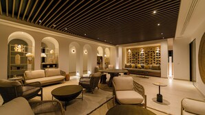 A spacious lounge area with a modern design, featuring a central seating area with sofas and chairs, a round coffee table, and a bookshelf with decorative items. - The NINE Lifestyle Experience (La Marsa)