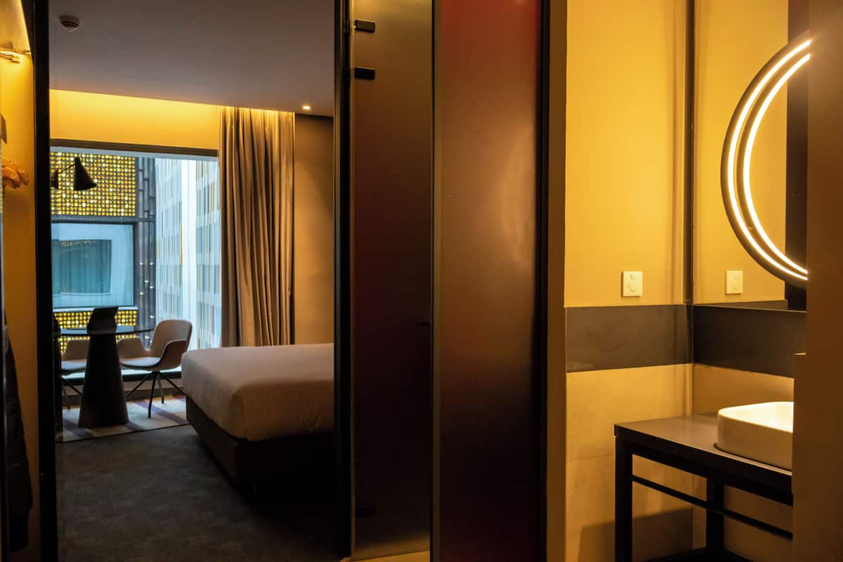 Ein Hotelzimmer mit Bett, Schreibtisch, Stuhl und Badezimmer mit Spiegel und Waschbecken.
