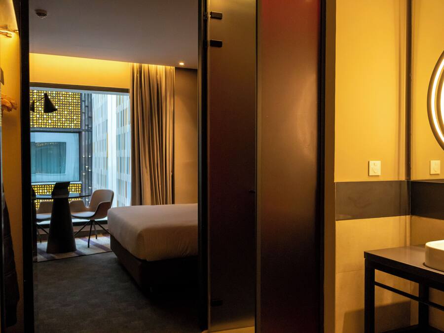Een hotelkamer met een bed, een bureau, een stoel en een badkamer met een spiegel en wastafel.