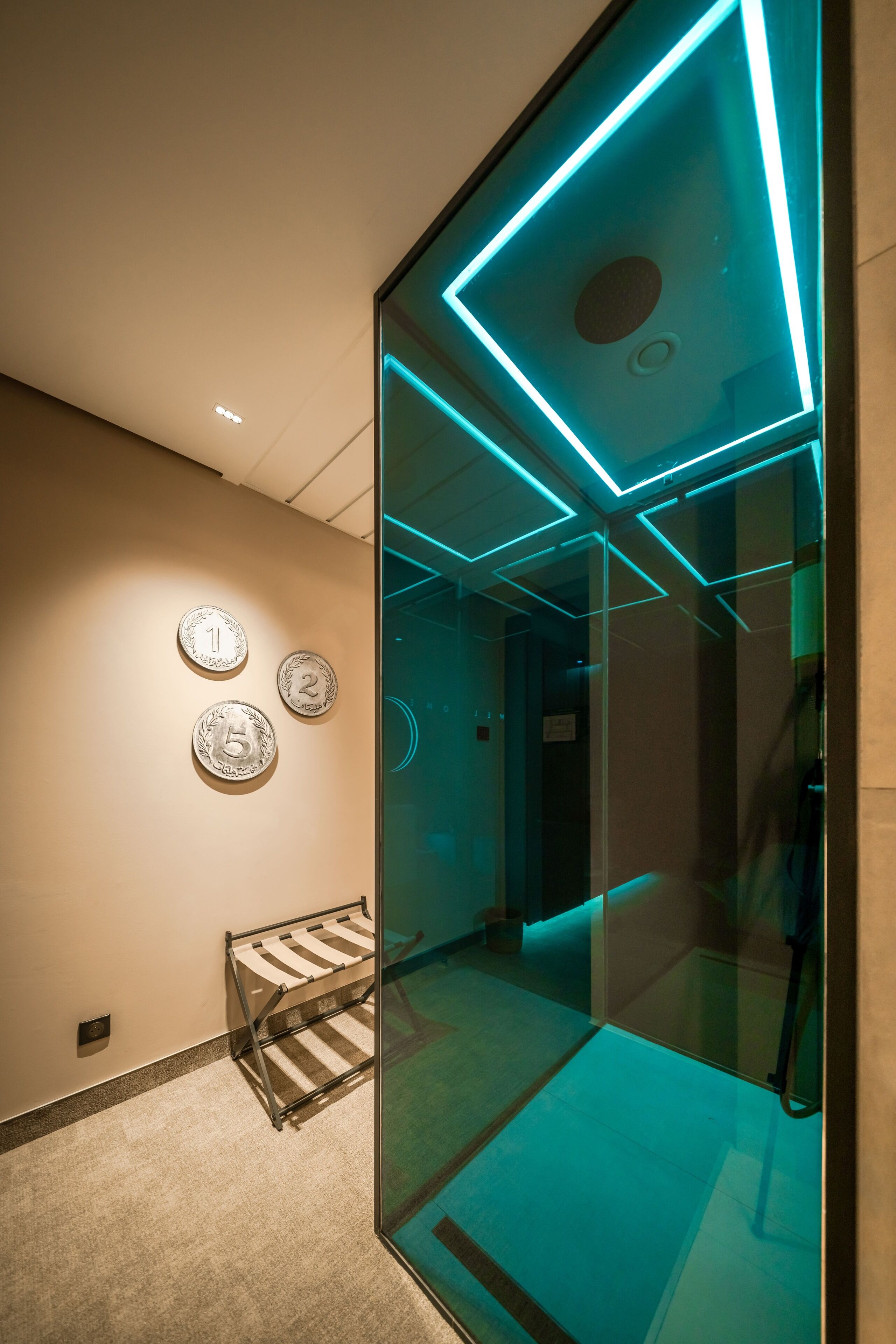 A modern hallway with a glass partition, a metal rack, and three numbered wall plates.