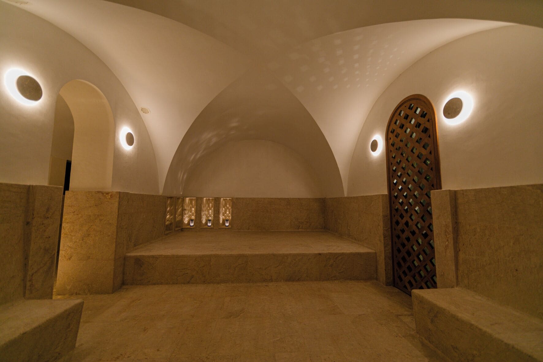 A spa room with a curved ceiling, a wooden lattice partition, and a stone bench.