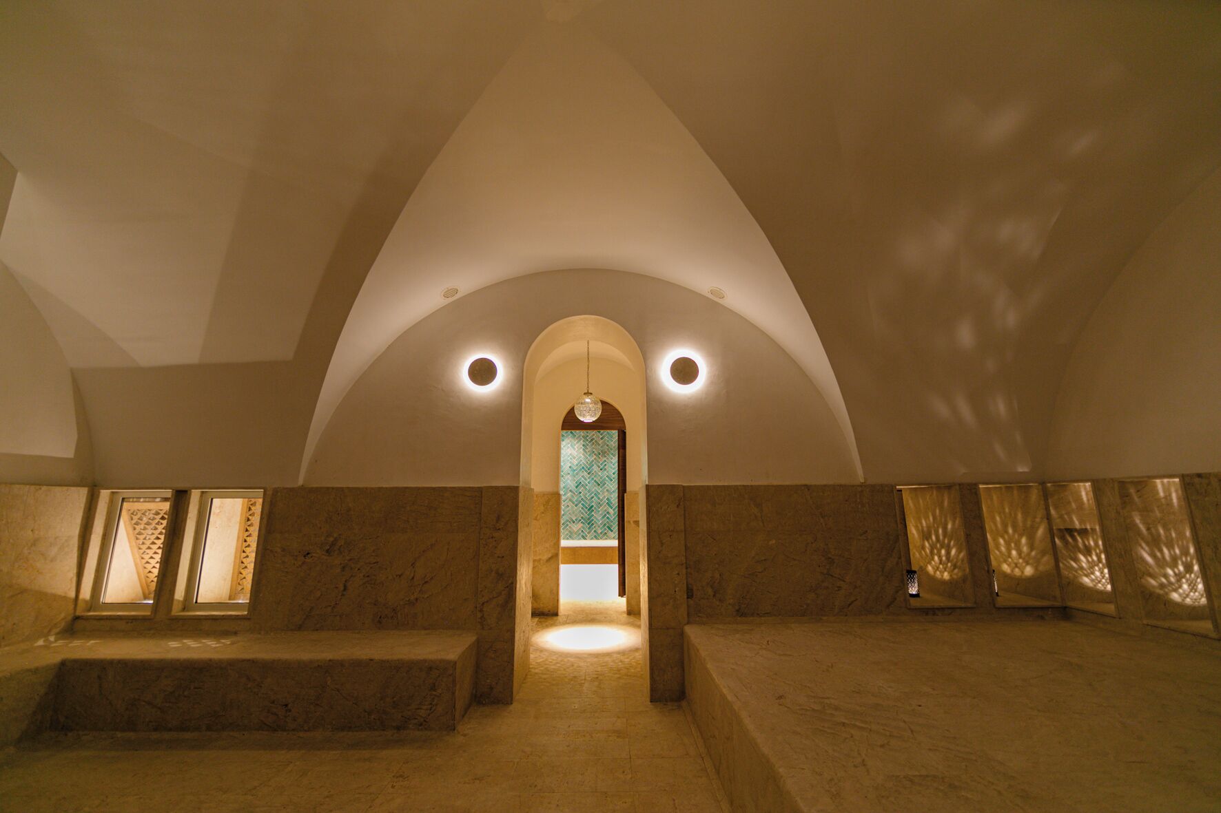 A spacious interior with a high arched ceiling, a central doorway, and a patterned wall at the far end.