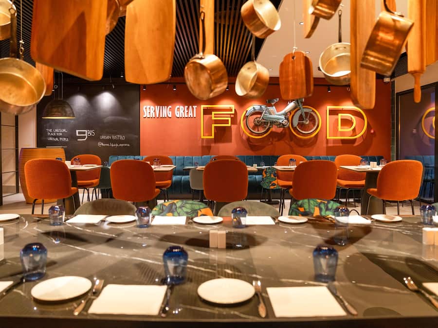 Un restaurante con una larga mesa de comedor lista para una comida, rodeada de sillas color naranja.