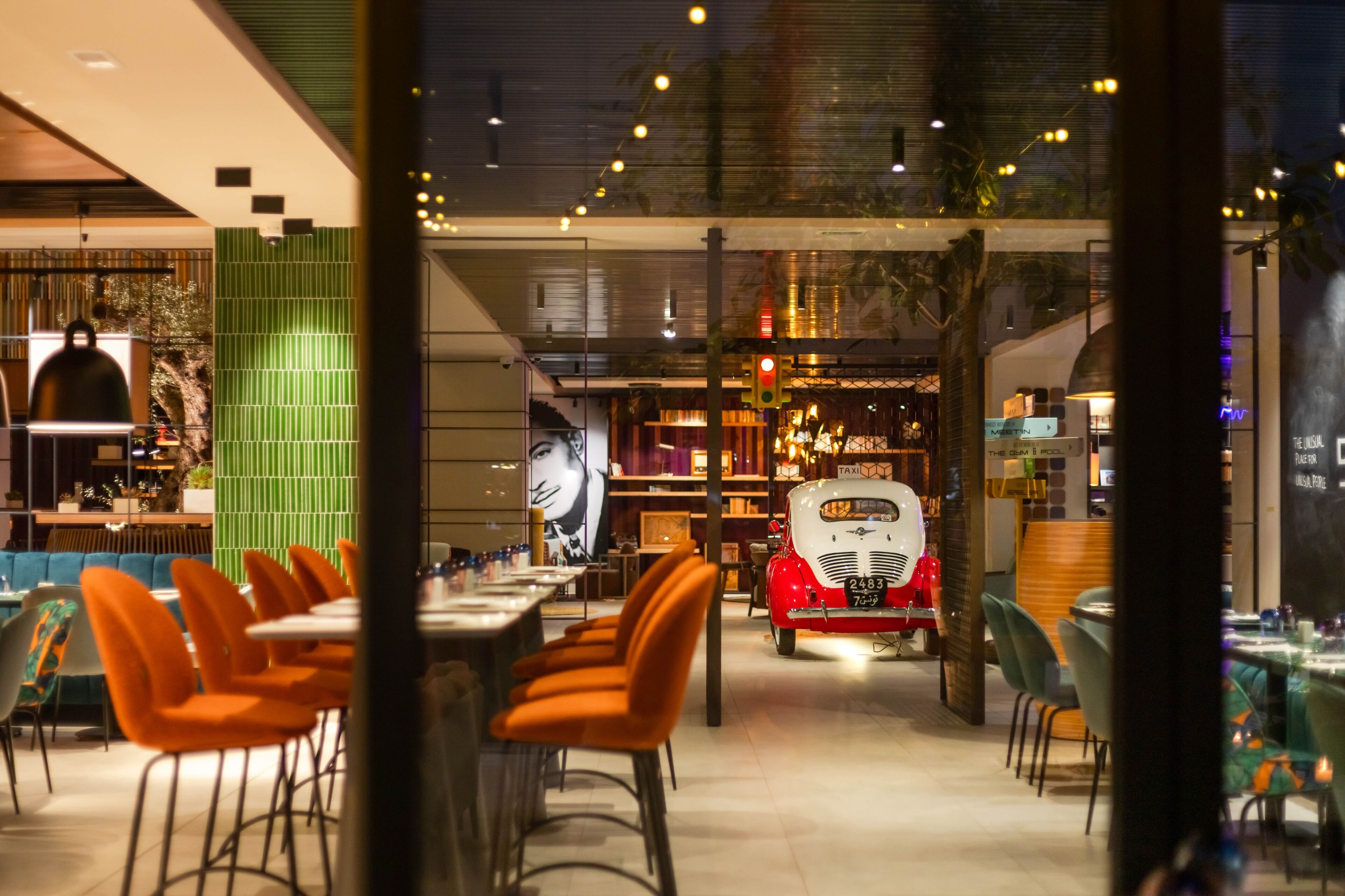 Un interno di ristorante moderno con sedie arancioni, una vetrina di auto d'epoca e una parete verde.