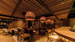 A restaurant with a modern interior, featuring wooden ceiling panels, woven light fixtures, and a variety of seating arrangements including tables and chairs. - The NINE Lifestyle Experience (La Marsa)