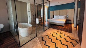 A modern hotel room with a large bed, a separate bathroom with a bathtub, and a glass partition. - The NINE Lifestyle Experience (La Marsa)