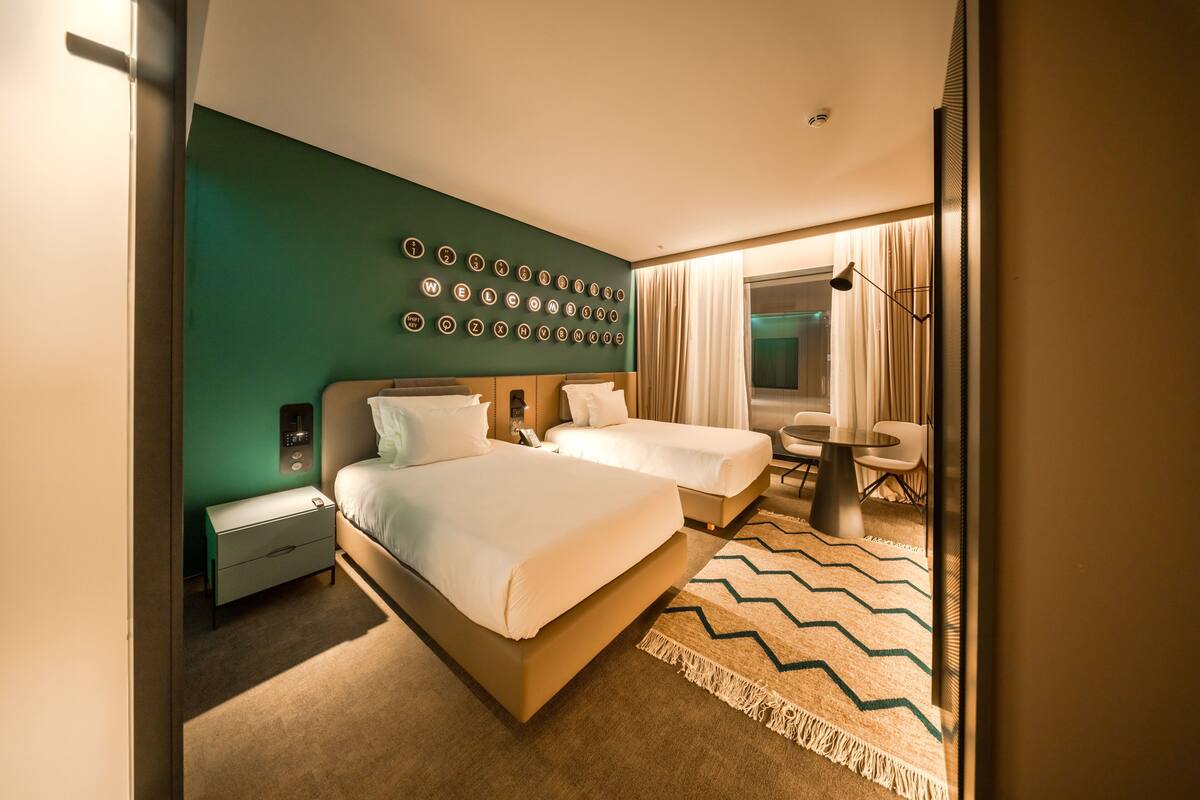 Ein Hotelzimmer mit zwei Betten, einem Schreibtisch, einem Stuhl, einer Wanduhr und einem Spiegel.