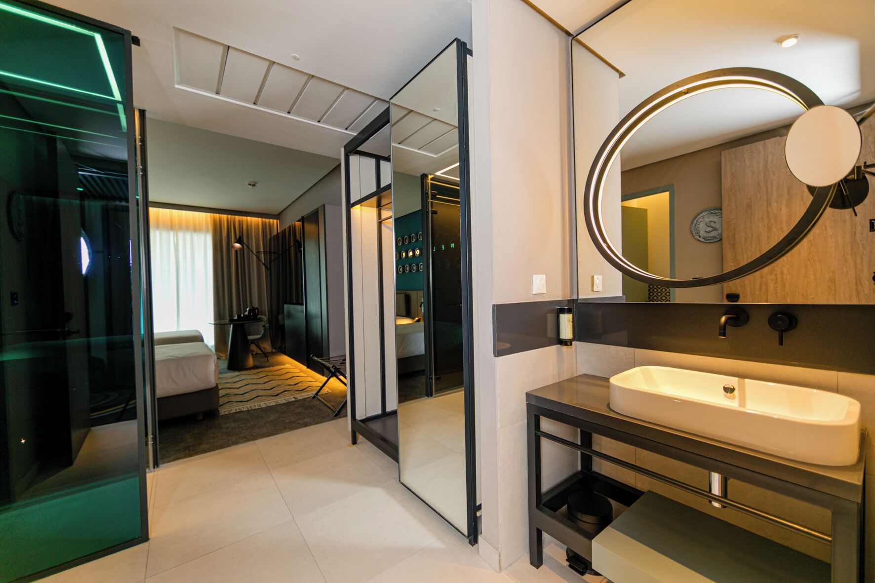 Habitación de hotel moderna con separador de vidrio, un espejo grande, un lavamanos y una cama.