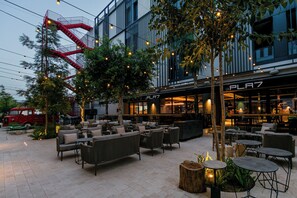 An outdoor seating area with wicker furniture and string lights, a red fire escape, and a building with a 'LA PLA7' sign. - The NINE Lifestyle Experience (La Marsa)