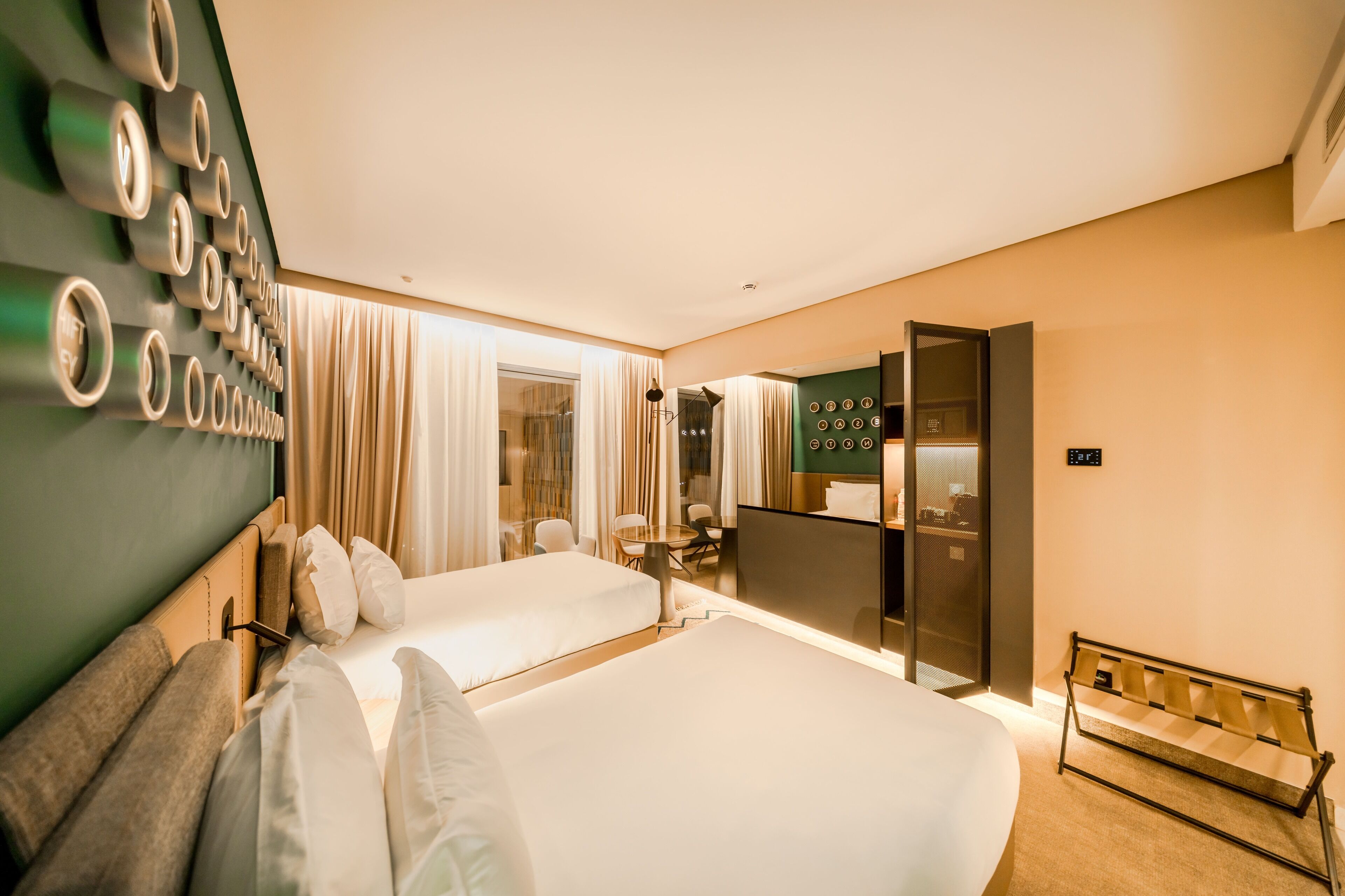 A hotel room with two beds, a seating area with a table and chairs, a mirror, and a bench.