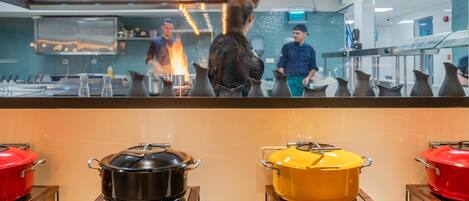 A kitchen area with pots on display, a chef in the background, and a counter with a menu.
