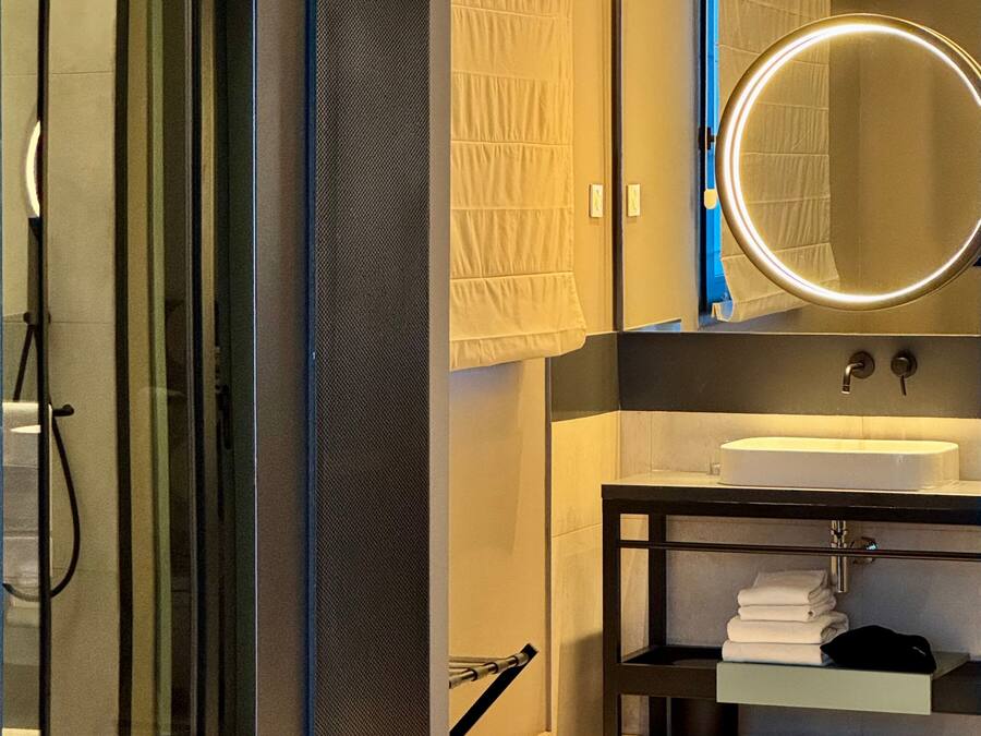 A modern bathroom with a glass shower enclosure, a round mirror, a white sink, and a towel rack.