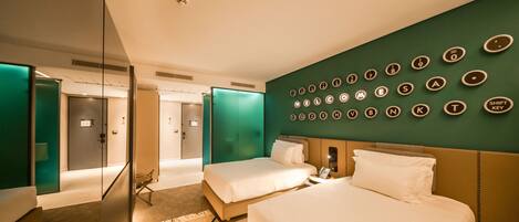 Habitación de hotel con dos camas, una pared de acento verde, un teclado montado en la pared y un panel de vidrio.