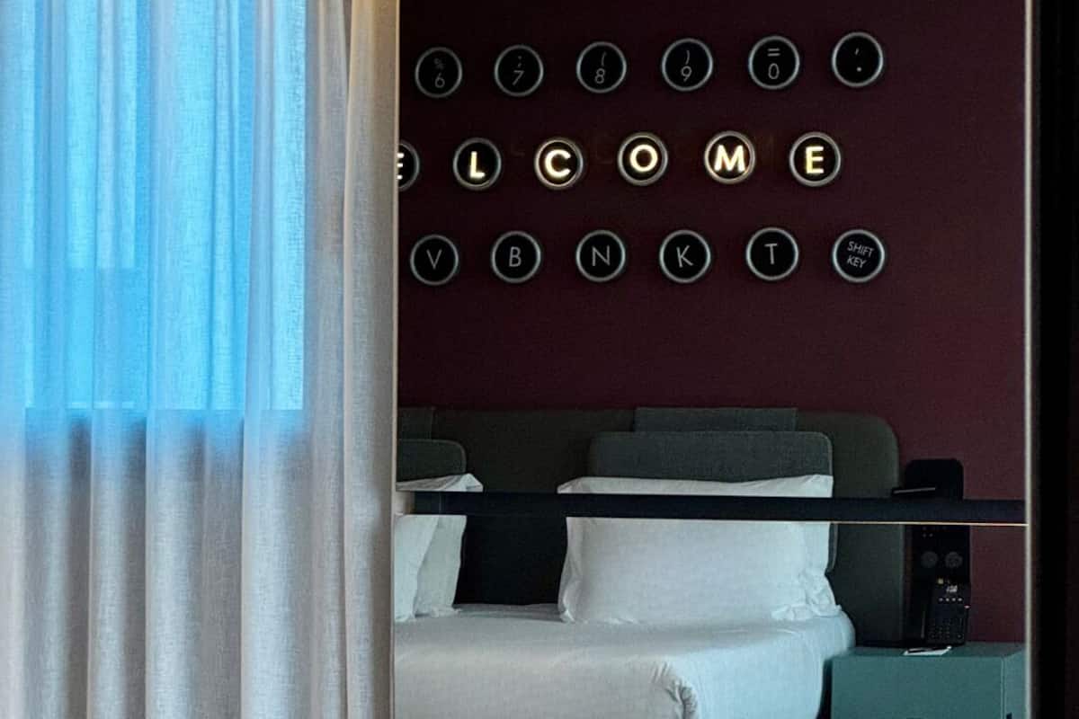 Ein Hotelzimmer mit einem Bett, einem Nachttisch, einem Tisch und einer Wand mit beleuchteten Willkommensbuchstaben.